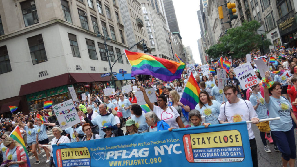 crowd of people on the street in NYC wearing PFLAG shirts and holding pride flags