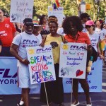 parents and transgender daughter smiling and looking at the camera, holding PFLAG signs